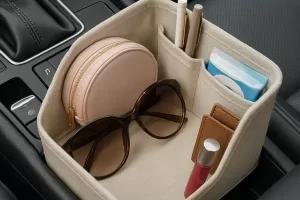 Organizador feminino no console central do carro com óculos de sol, bolsinha rosa, batom e itens essenciais.