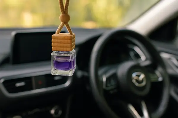 Close-up do interior de um carro decorado com elementos delicados e femininos, com um aromatizador pendurado no retrovisor.