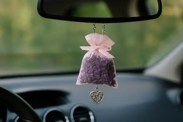 Sachê perfumado com flores secas roxas pendurado no retrovisor de um carro, com pingente de coração prateado.